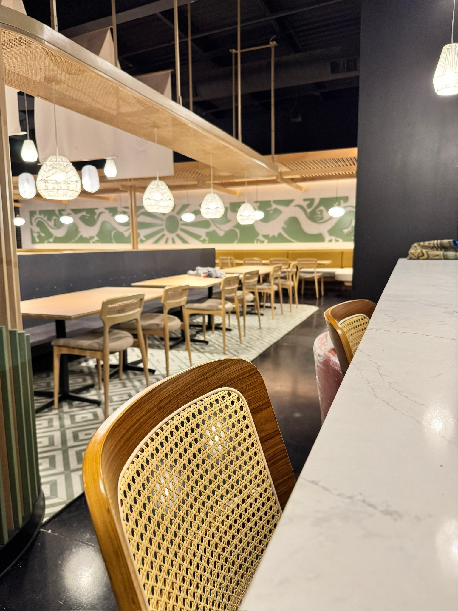 Ginsoy Houston — view from the marble bar towards the dining floor with cane-back chairs and the wave-pattern green mural