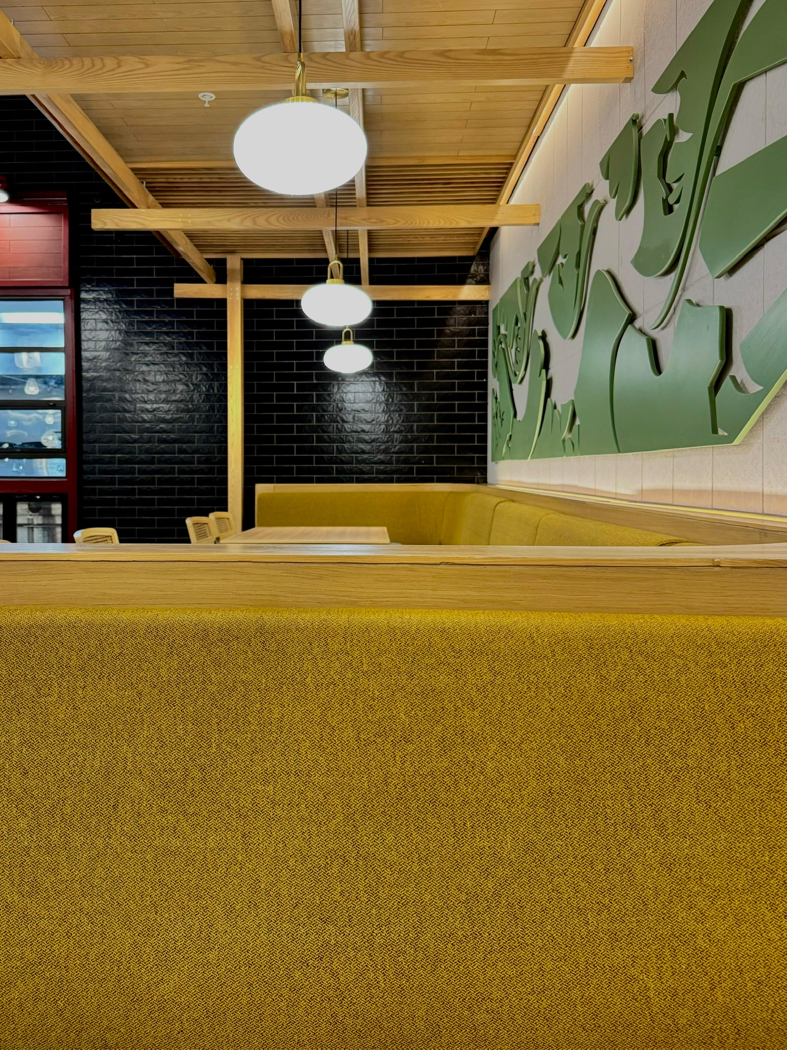 Ginsoy Houston — mustard-yellow upholstered banquette under suspended globe pendants and a wooden ceiling raft